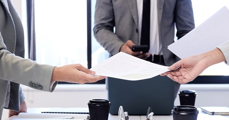 Documents change hands during a business meeting of three people