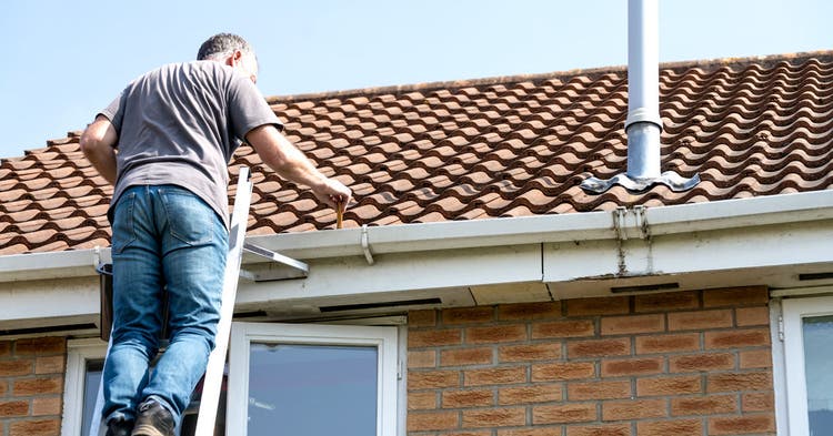 Man on a ladder cleaning gutters