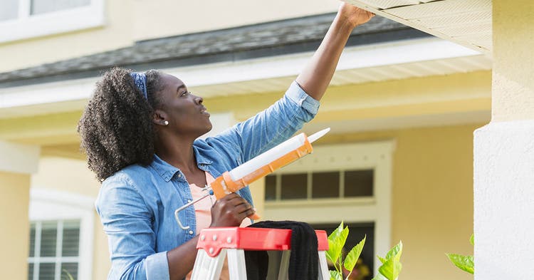 Black female homeowner caulks exterior roof of home