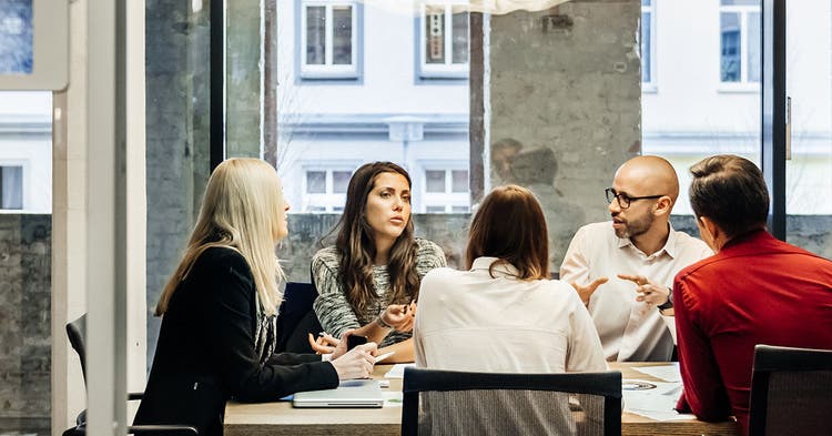 Five people have a discussion in a conference room