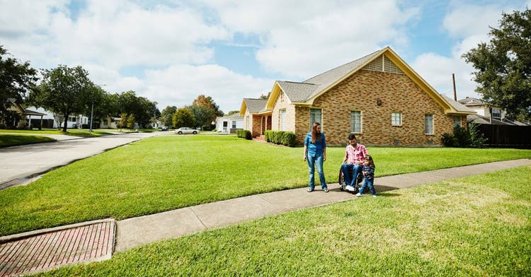 Man on wheelchair strolls though neighborhood with family