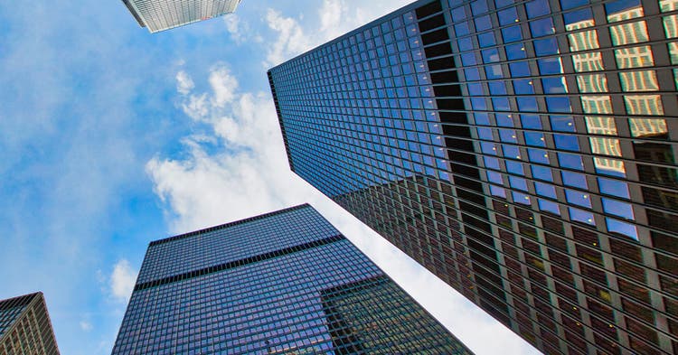 Looking up between 3 glass commercial buildings against a blue sky