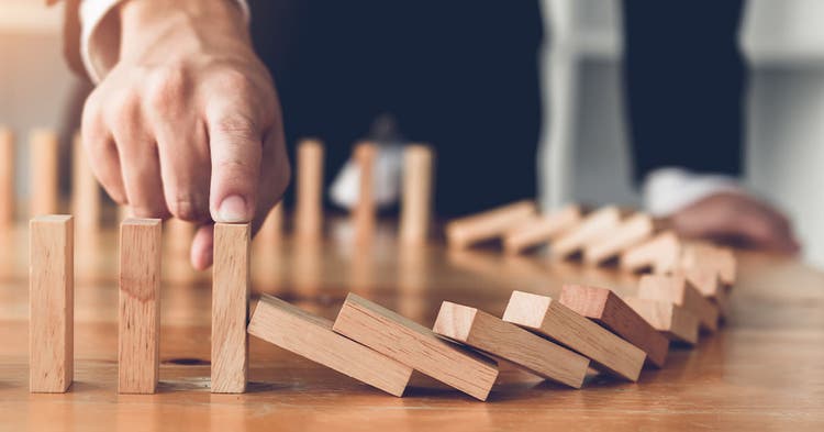 Finger stopping wooden block from falling in the line of domino